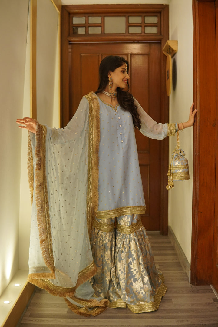 Elegant mehndi outfit set including embroidered gharara, festive potli, khussa flats, and jewelry accessories.