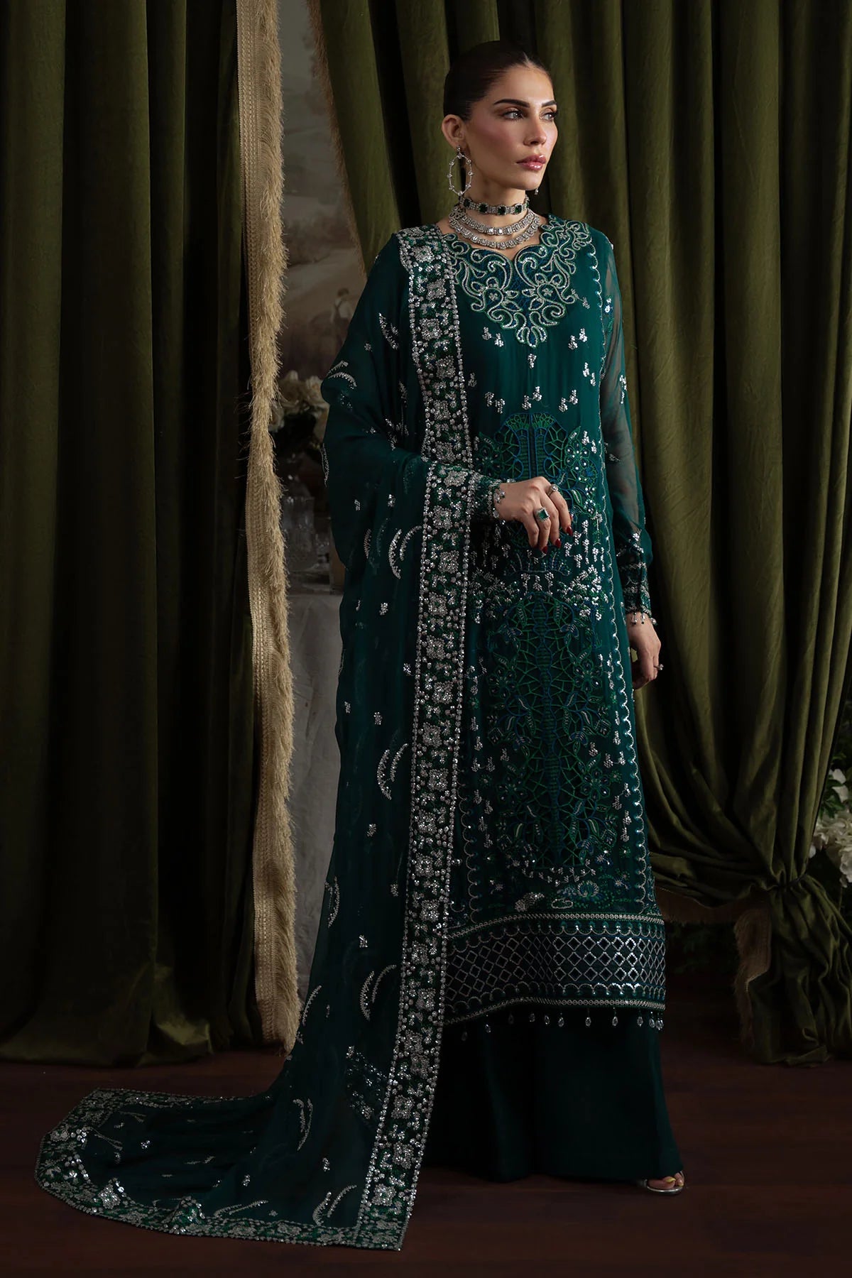 Model wearing deep green embroidered chiffon suit with heavily embellished dupatta in an elegant standing pose