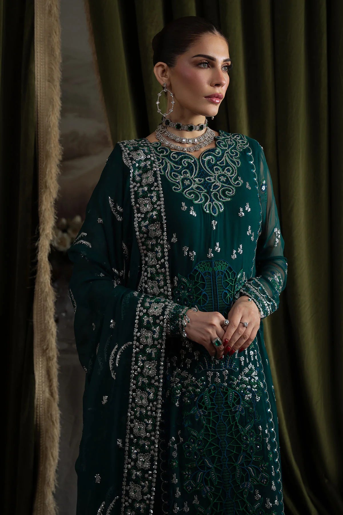 Model gazing sideways in green embroidered chiffon outfit with intricate silver embellishments and choker necklace