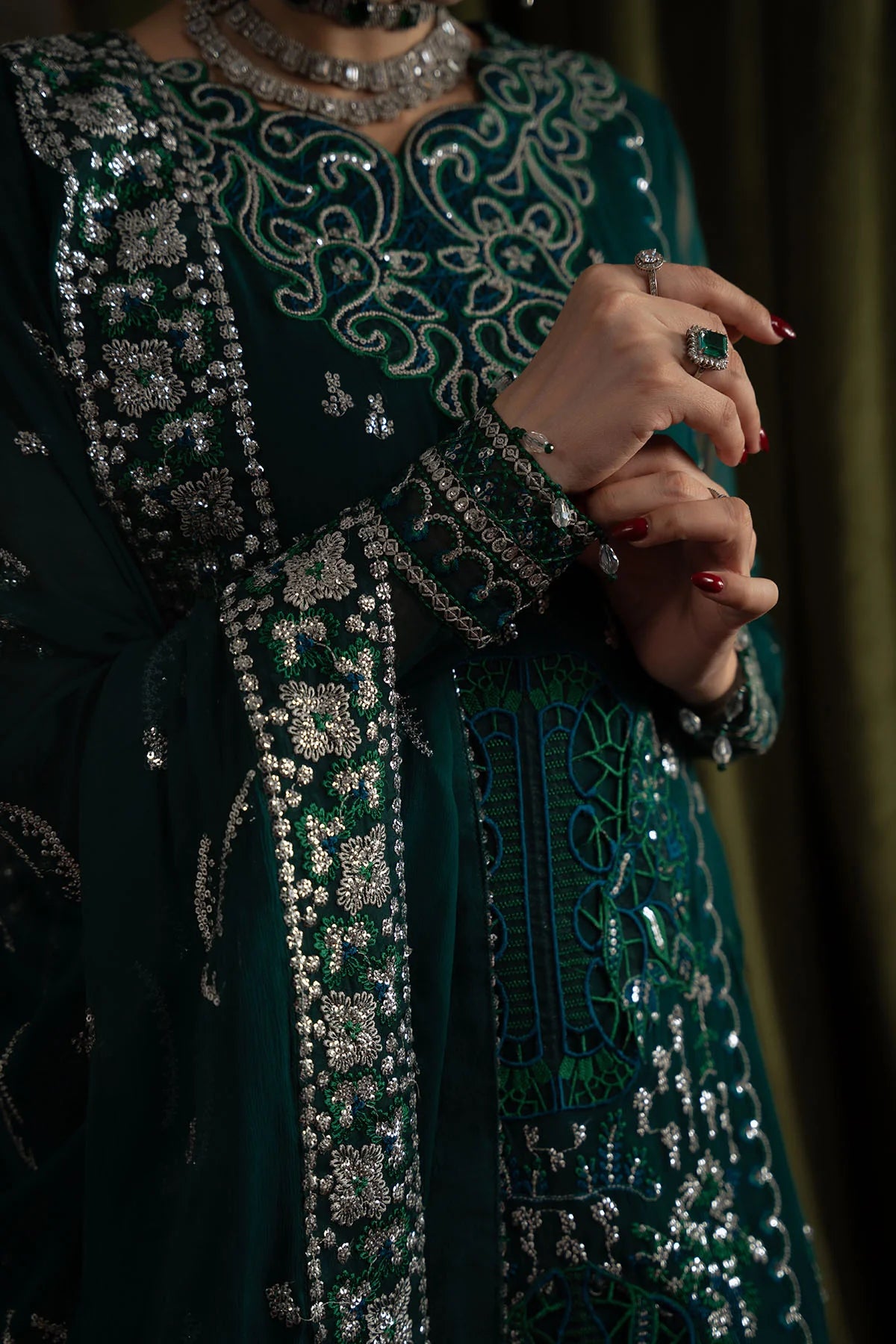 Close-up of embroidered sleeve and border details on deep green chiffon fabric with intricate silver work